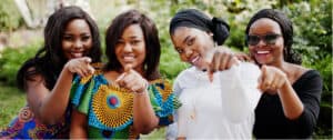 Diverse women smiling and pointing at the camera outdoors.